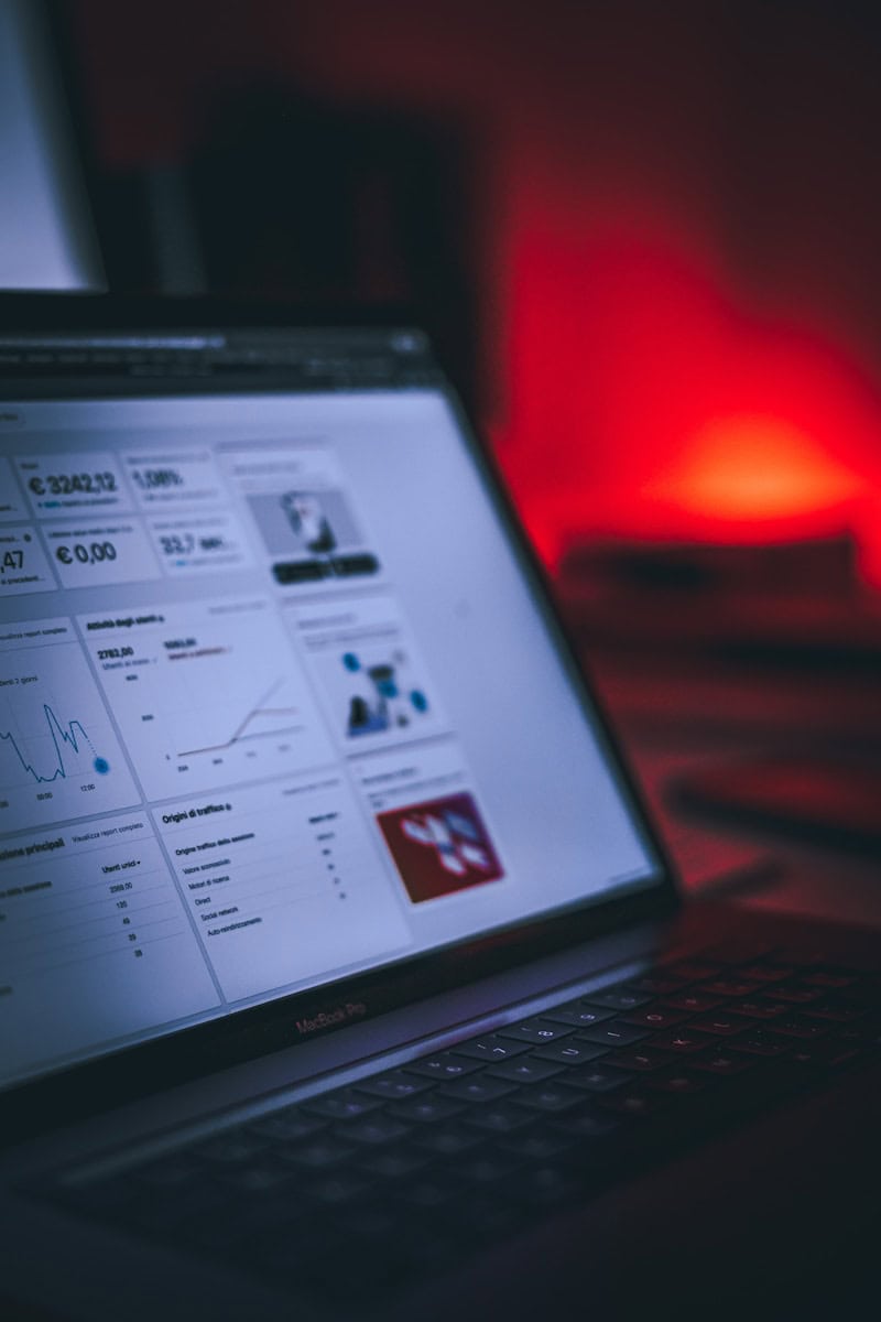 A laptop displaying financial data and graphs on its screen, with a blurred red light in the background—perfect for creating an explainer video on topics like finance or on-page SEO optimization. turned-on MacBook Pro